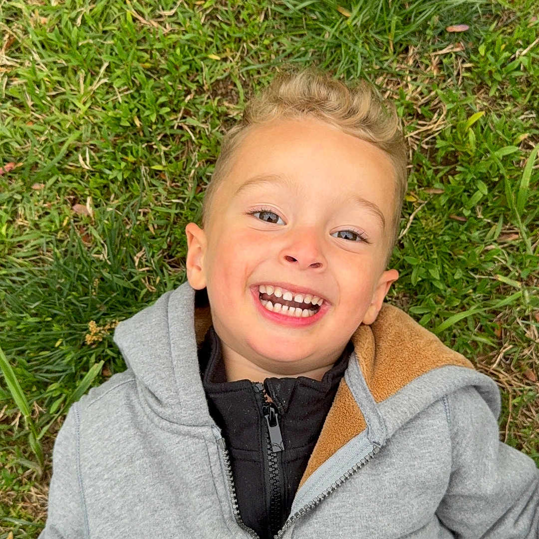 Patrick joined the competition — help win amazing prizes! child, boy, smiling, happy, laughing, portrait, outdoor, grass, lying_down, face, teeth, blond_hair, jacket, hoodie, zipper, nature, garden, close_up, daylight, casual_clothing