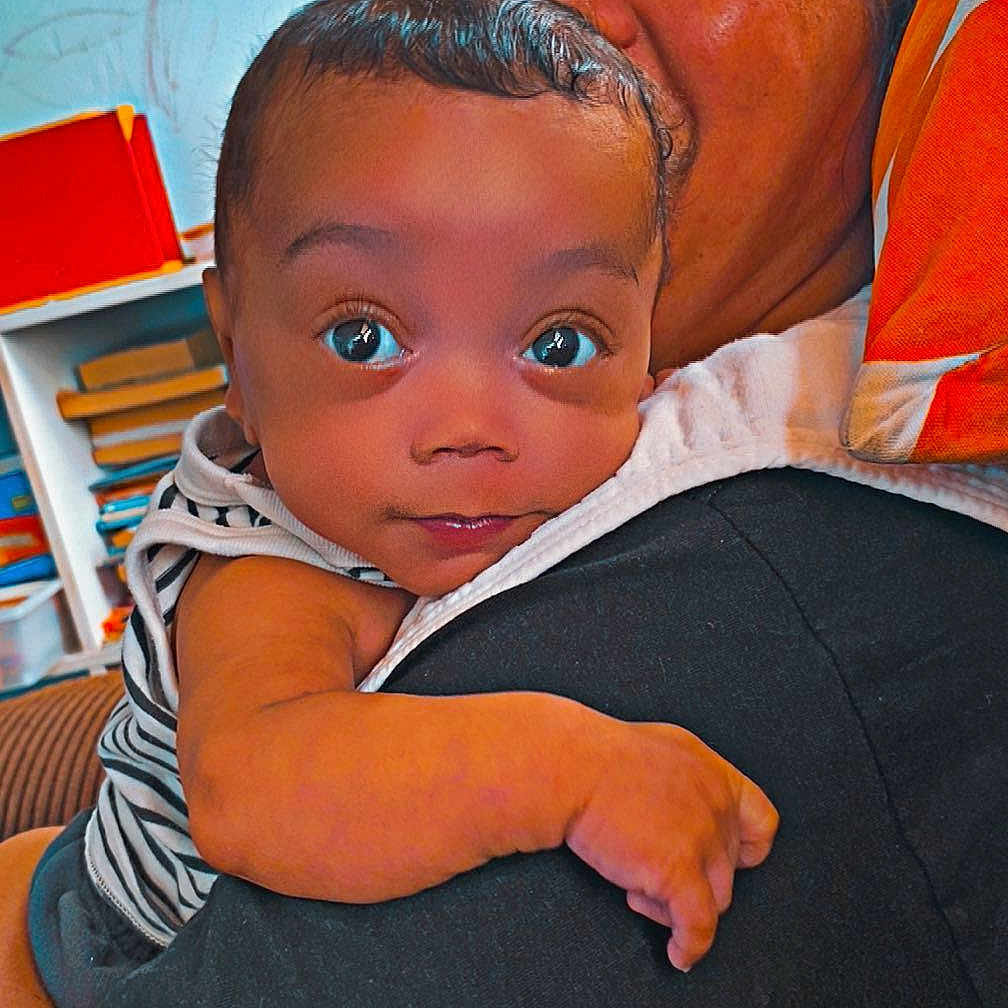 Carson is registered to the contest to win money with this photo: adult, arm, baby, books, child, comfort, cuddle, eyes, face, furniture, hand, head, holding, indoor, person, pillow, shelf, skin, striped_clothing, wall