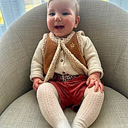 Céleste a rejoint le concours — aidez-le/la à gagner de superbes lots ! baby, child, smile, happy, armchair, clothing, vest, knitted_tights, tights, indoor, person, infant, cute, face, sitting, window, natural_light, cozy, warm_clothing, blinds