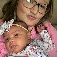 Mckinlee is registered to the contest to win money with this photo: baby, child, closeup, couch, expression, face, family, floral_clothing, glasses, head, headband, holding, indoor, love, person, pink_shirt, portrait, skin, smile, woman