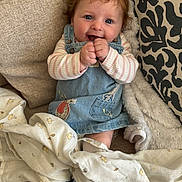 Isla-Ro is registered to the contest to win money with this photo: baby, blanket, blue_eyes, child, couch, cozy, curly_hair, cute, denim_dress, fabric, happy, indoor, person, plush_blanket, portrait, seated, smiling, socks, soft_texture, striped_shirt