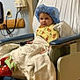 Malachi joined the competition — help win amazing prizes! child, hospital, chair, blanket, surgical_cap, gown, medical, indoor, person, pediatric, patient, healthcare, curious, seated, footwear, red_socks, medical_equipment, bedside, hospital_room, wood_floor