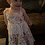 child, girl, dress, floral_pattern, pigtails, hair_bows, smile, indoor, couch, wooden_floor, slippers, person, young_child, cute, standing, portrait, furniture, home, happy, clothing