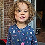 child, toddler, curly_hair, pajamas, smiling, face, portrait, outdoor, brick_wall, door, floor, toy_car, home, cute, person, young_child, happy, clothing, casual, daylight