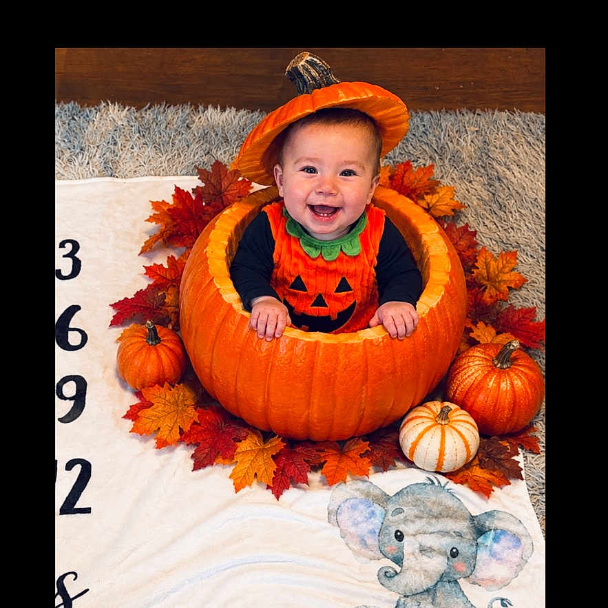 Maverick is registered to the contest to win money with this photo: baby, child, halloween, pumpkin, pumpkin_costume, autumn, fall_leaves, orange, smiling, happy, portrait, indoor, blanket, elephant, nursery, seasonal, costume, sitting, festive, photography
