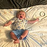 baby, infant, smiling, lying_down, blanket, numbers, blue_shorts, patterned_shirt, happy, arms_spread, face, head, skin, feet, hands, marker, months, indoors, cozy, cute