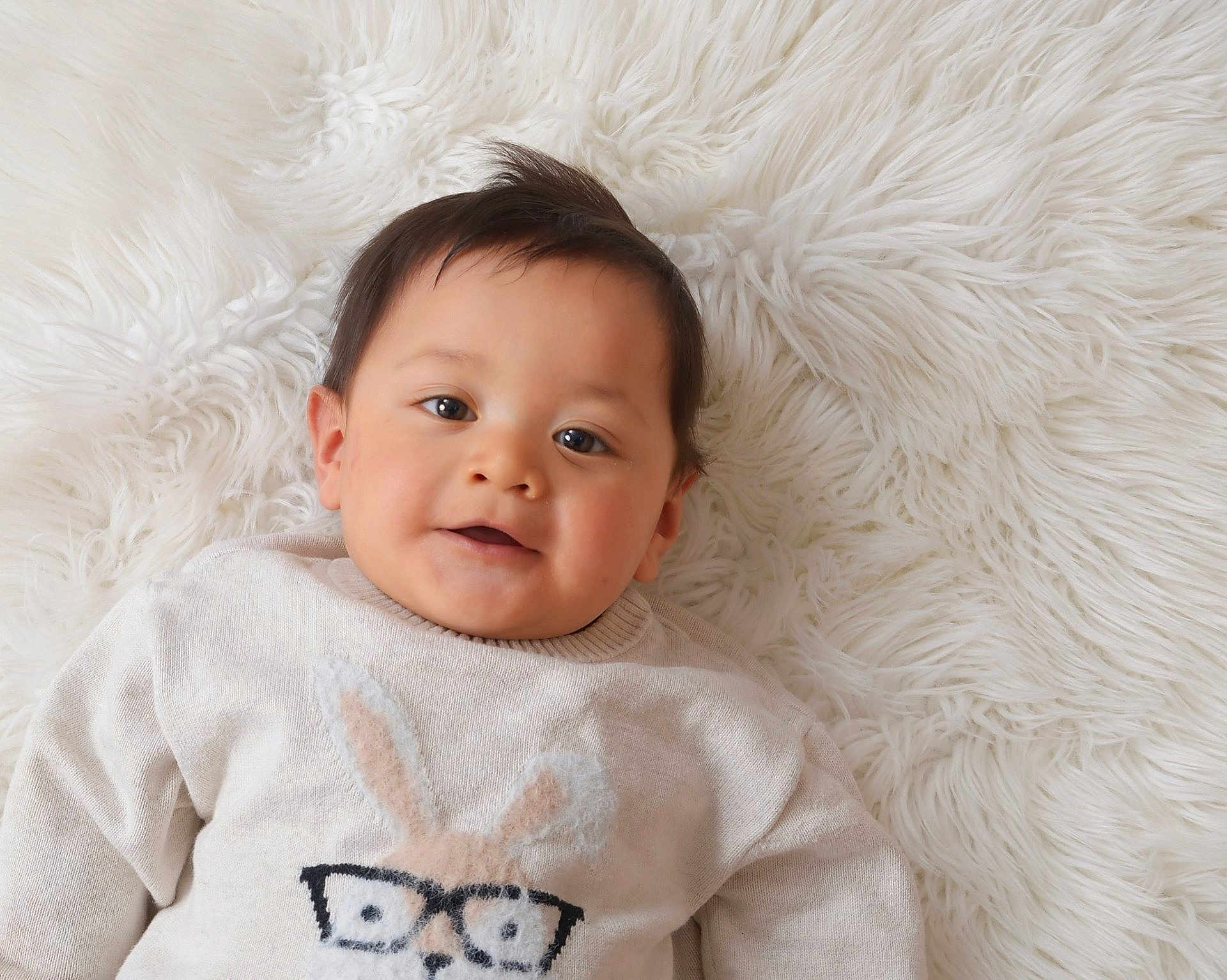 Maximus is registered to the contest to win money with this photo: baby, child, smiling, sweater, bunny, glasses, cute, portrait, infant, lying_down, white_background, fluffy_rug, soft_texture, warm_clothing, young_child, indoors, happy, face, cozy, comfortable