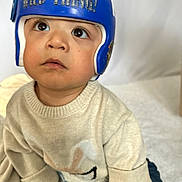 Maximus is registered to the contest to win money with this photo: toddler, child, helmet, blue_helmet, sweater, beige_sweater, curious_look, indoors, closeup, baby, cute, sitting, soft_surface, casual_clothing, portrait, headgear, expression, young_child, innocence, face