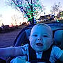 Sage is registered to the contest to win money with this photo: baby, child, car_seat, blanket, smile, happy, outdoor, tree, lights, holiday_lights, evening, dusk, nature, person, infant, face, clothing, park, seat_belt, joy