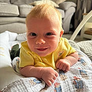 Nancy joined the competition — help win amazing prizes! baby, child, smiling, yellow_shirt, blanket, indoor, face, hands, couch, home, cute, infant, portrait, toddler, patterned_blanket, cozy, happy, closeup, relaxed, light