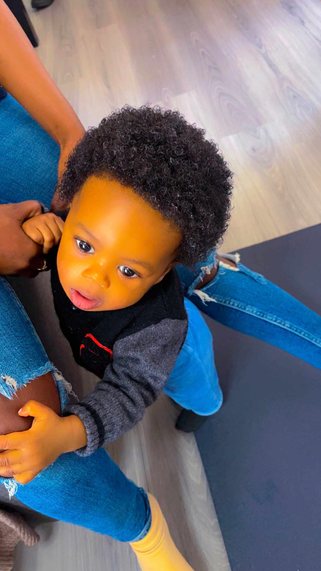 Noah a rejoint le concours — aidez-le/la à gagner de superbes lots ! toddler, child, curly_hair, indoor, floor, jeans, hand, leg, sweater, black_clothing, person, skin, footwear, yellow_sock, denim, casual, cute, exploring, holding, candid