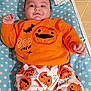 baby, infant, child, orange_clothing, pumpkin_pattern, halloween, bat, polka_dot_blanket, diapers, smiling, cute, lying_down, indoors, toddler, face, person, happy, clothing, bed, blanket