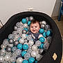 baby, ball_pit, blue_balls, white_balls, silver_balls, smiling, child, indoor, floor, black_cushion, happy, cute, person, toy, play, head, face, infant, home, cozy