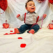 Kyree joined the competition — help win amazing prizes! child, baby, infant, smiling, barefoot, suspenders, striped_shirt, jeans, heart_balloon, valentine_decor, red_beads, tinsel, white_backdrop, rose_petals, party, portrait, celebration, indoor, cheerful, balloon