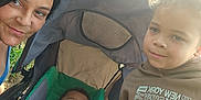 Kyree is registered to the contest to win money with this photo: baby, casual_clothing, child, curly_hair, daylight, expression, fabric, face, family, green, hoodie, nature, outdoor, parent, person, portrait, smile, stroller, woman, young_boy