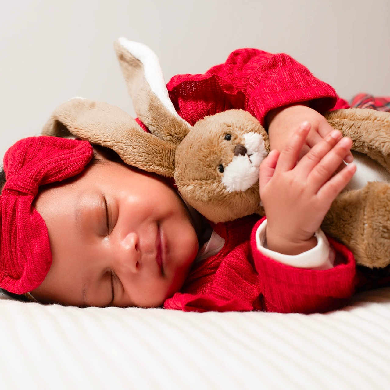 Abygaëlle a rejoint le concours — aidez-le/la à gagner de superbes lots ! adorable, baby, bed, child, cozy, cuddling, cute, hands, headwear, indoors, infant, peaceful, plush_bunny, portrait, red_headband, red_sweater, relaxed, sleeping, soft_toy, white_bedspread