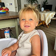 Eïra a rejoint le concours — aidez-le/la à gagner de superbes lots ! toddler, child, high_chair, blonde_hair, blue_eyes, smiling, indoor, kitchen, table, chair, fruit_bowl, milk_carton, wooden_floor, plant, white_clothing, happy, portrait, baby, furniture, home