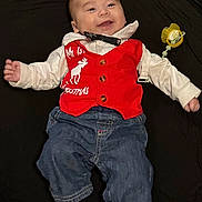 Oliver is registered to the contest to win money with this photo: baby, infant, smiling, vest, red_clothing, white_shirt, blue_jeans, pacifier, lying_down, holiday_clothing, reindeer, clothing_buttons, happy, child, indoors, cute, portrait, small_hands, fabric, black_background