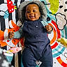 baby, infant, smiling, play_mat, colorful, overalls, clothing, face, happy, lying_down, child, toy, patterned, indoor, cute, person, toddler, blue_clothing, skin, playtime