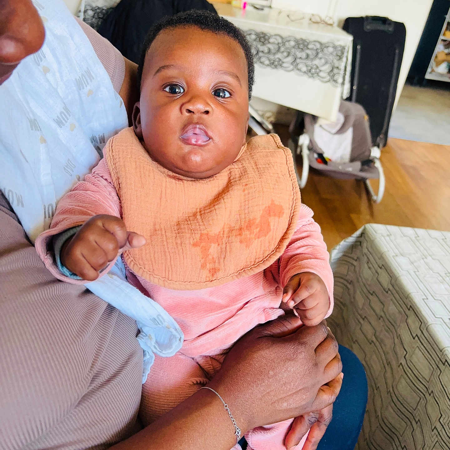 Elia participe au concours pour gagner de l'argent avec cette photo : baby, child, adult, holding, indoor, cozy, home, person, clothing, bib, pink, peach, face, hands, expression, seated, furniture, table, floor, background