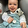 baby, child, smiling, blue_blanket, plush_toy, wolf_toy, car_seat, gray_background, happy, infant, cute, soft_texture, clothing, face, hand, portrait, seated, indoors, closeup, person