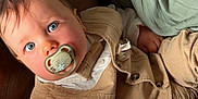 Sacha participe au concours pour gagner de l'argent avec cette photo : baby, pacifier, blue_eyes, beige_vest, white_shirt, tattoo, soft_fabric, green_fabric, infant, close_up, portrait, child, cute, indoors, relaxed, hand, face, clothing, person, skin