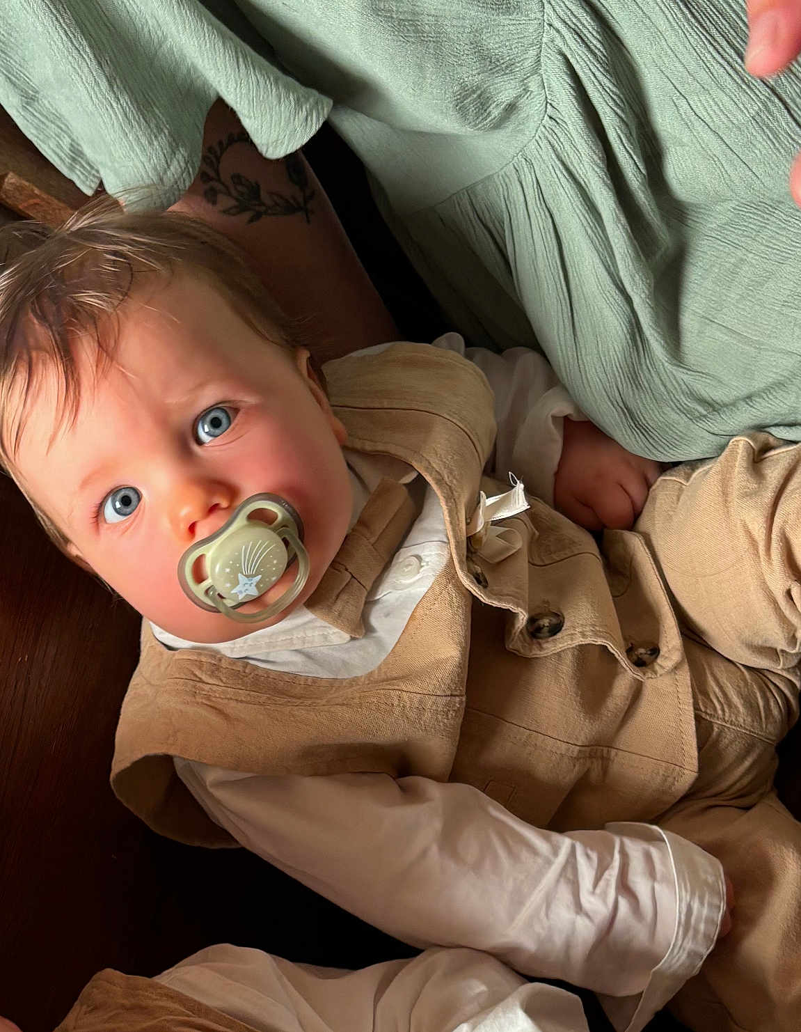 Sacha participe au concours pour gagner de l'argent avec cette photo : baby, pacifier, blue_eyes, beige_vest, white_shirt, tattoo, soft_fabric, green_fabric, infant, close_up, portrait, child, cute, indoors, relaxed, hand, face, clothing, person, skin