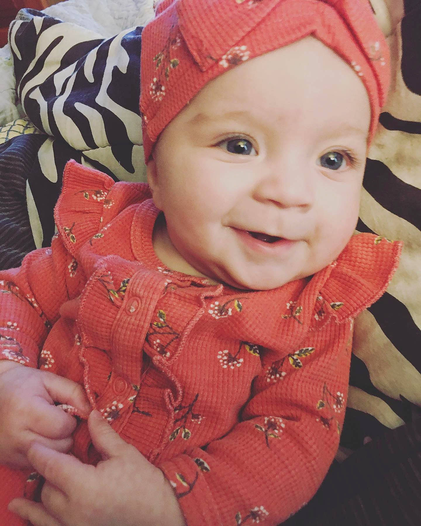 Alexandra is registered to the contest to win money with this photo: baby_toddler_clothing, cap, cheek, chin, eye, face, facial_expression, happy, head, headgear, headwear, human, iris, lip, nose, organ, person, pink, skin, sleeve