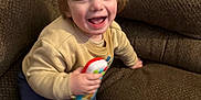 Gavin joined the competition — help win amazing prizes! toddler, child, toy, couch, brown_couch, happy, smiling, indoors, casual_clothing, sweater, pants, playful, young_child, person, face, hair, seated, home, furniture, joyful