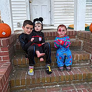 Gavin is registered to the contest to win money with this photo: child, children, costume, halloween, face_paint, pumpkin, brick, steps, door, house, porch, socks, mickey_mouse, pajamas, outdoor, fall, leaf, smiling, sitting, group