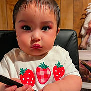 Azalea joined the competition — help win amazing prizes! toddler, child, indoor, chair, wood_paneling, white_shirt, strawberry_print, bow, hair_accessory, comb, colorful_pants, serious_expression, cute, person, sitting, young_child, black_chair, short_hair, close_up, portrait