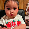 toddler, child, indoor, chair, wood_paneling, white_shirt, strawberry_print, bow, hair_accessory, comb, colorful_pants, serious_expression, cute, person, sitting, young_child, black_chair, short_hair, close_up, portrait