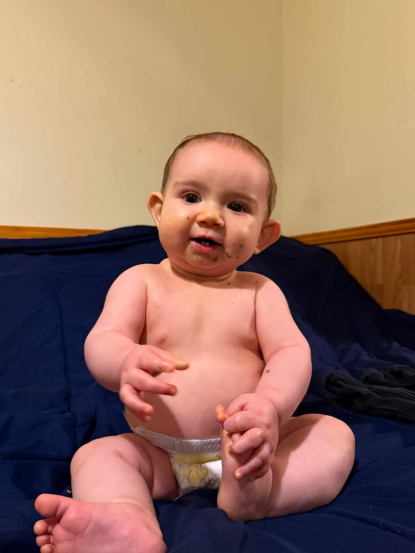 Jameson joined the competition — help win amazing prizes! baby, diaper, infant, sitting, bed, blue_bedspread, food_smudges, cute, chubby, hand, foot, skin, face, expression, curious, indoors, wood_paneling, wall, child, young