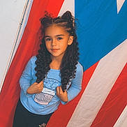 Myrelis Gonzalez joined the competition — help win amazing prizes! child, girl, portrait, smiling, curly_hair, long_hair, blue_shirt, black_pants, standing, flag, patriotic, indoors, wooden_floor, door, red_white_blue, fashion, pose, photography, young_person, safe