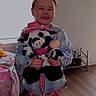 child, girl, smiling, plush_toy, cow, hat, pajamas, pink, bedroom, window, floor, toy, clothing, happy, person, indoor, furniture, bed, shoes, warm