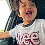 child, smiling, happy, curly_hair, tshirt, lee_logo, car_interior, window, seat, person, portrait, casual_clothing, young_child, joyful, laughing, daylight, human_face, mouth_open, teeth, arm