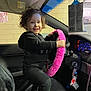 Zelyiana is registered to the contest to win money with this photo: child, toddler, car_interior, steering_wheel, pink_steering_wheel_cover, curly_hair, black_clothing, smiling, car_seat, dashboard, keys, rearview_mirror, garage_wall, window, footwear_off, happy, indoors, toy_like_object, person, playful