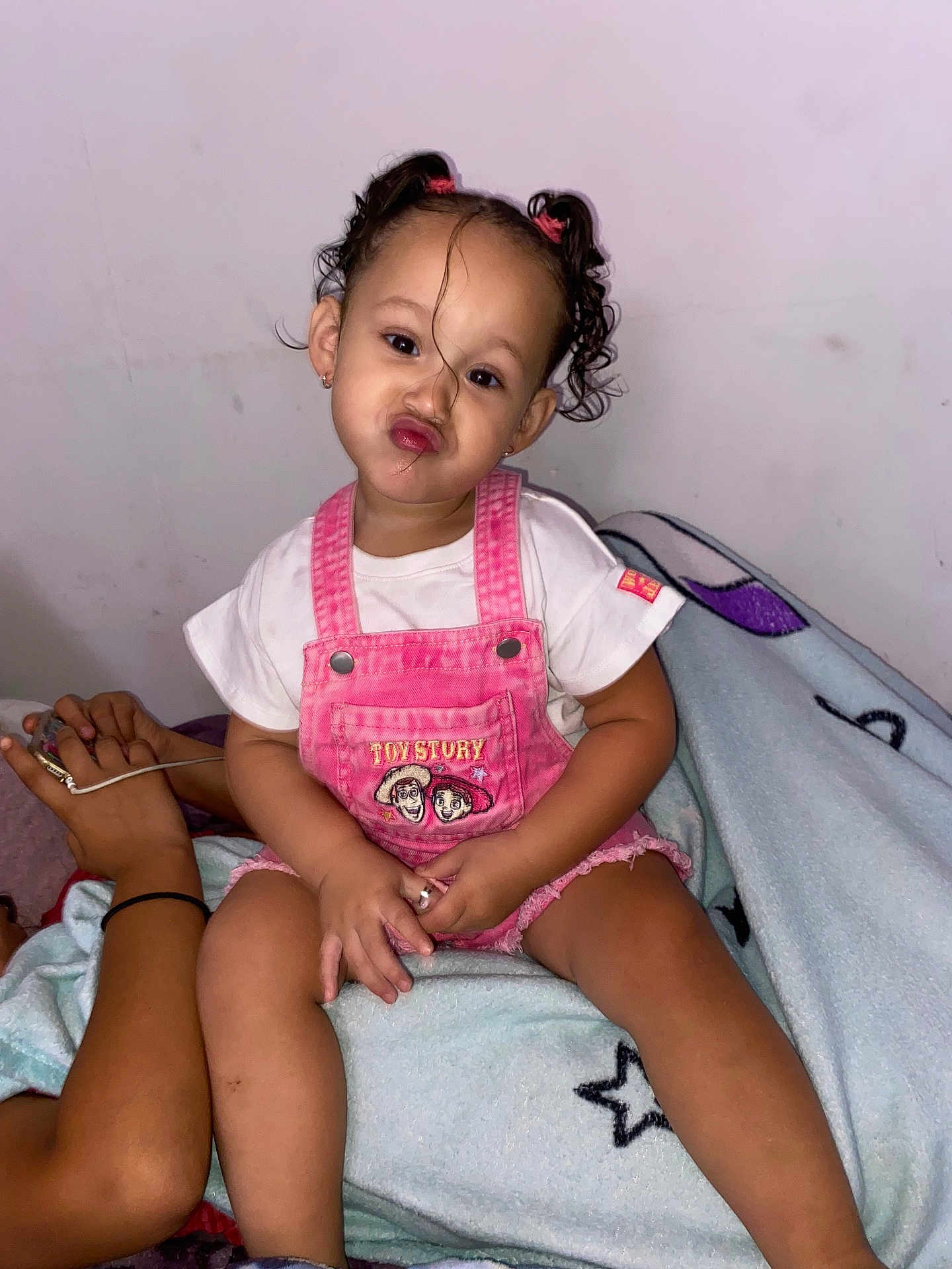 Zelyiana joined the competition — help win amazing prizes! toddler, child, girl, pigtails, curly_hair, pink_overalls, toy_story, white_tshirt, blanket, indoor, playful_expression, sitting, cute, person, skin, furniture, hand, relaxed, casual, portrait