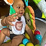 Djuantay joined the competition — help win amazing prizes! baby, bib, child, colorful, curious, cute, hand, happy, indoor, infant, kiwi_toy, lion_print, orange_toy, person, plastic_balls, playful, playpen, sitting, smiling, toy