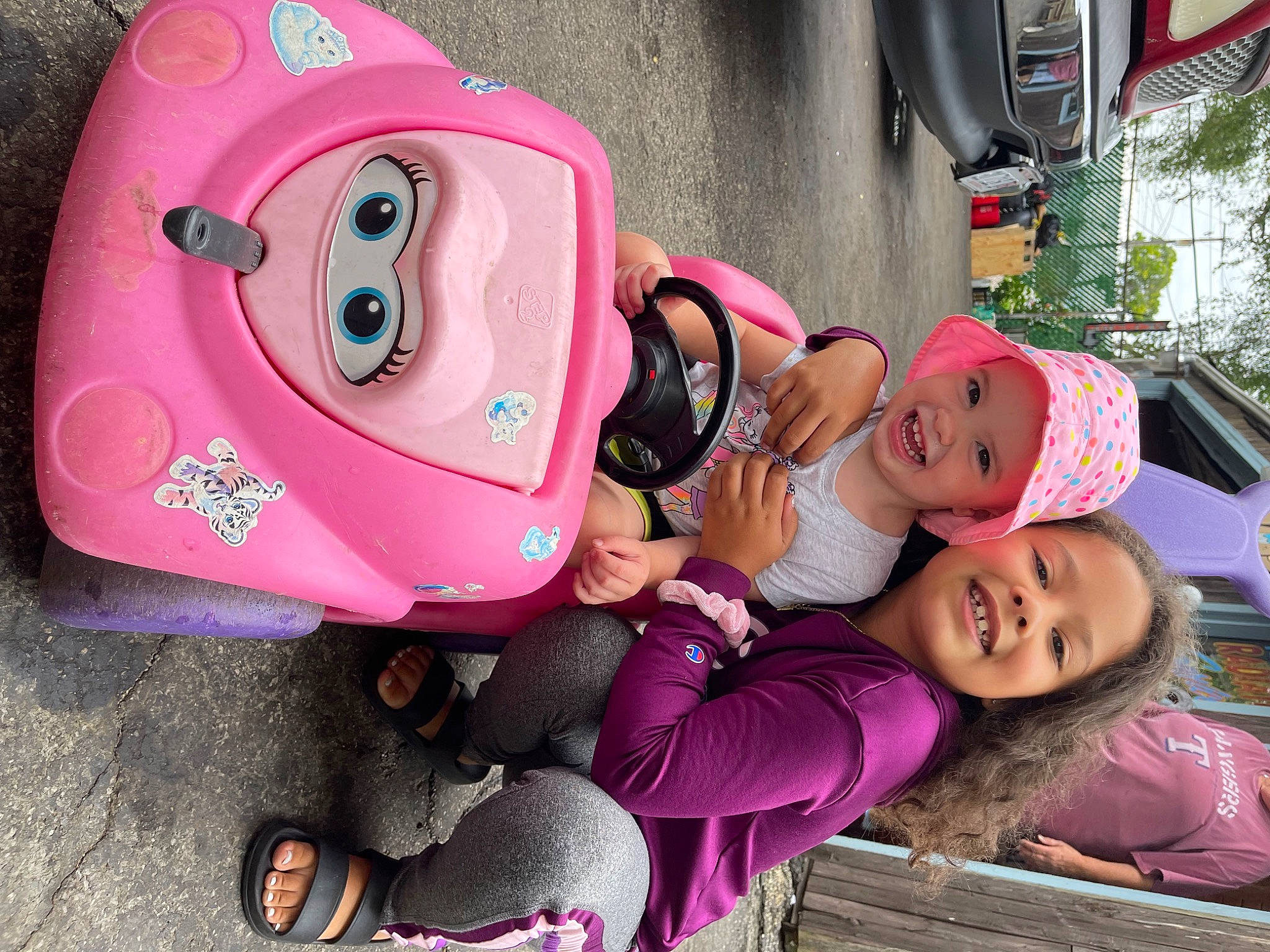 Frankie is registered to the contest to win money with this photo: automotive_design, car, child, cool, facial_expression, green, happy, hat, headgear, headwear, joy, leisure, motor_vehicle, mouth, person, pink, plant, red, smile, tire