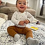 baby, child, smiling, sitting, indoor, carpet, rug, clothing, pants, shirt, socks, face, hands, person, home, couch, blurred_background, window, curtains, toy
