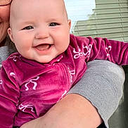 Emily is registered to the contest to win money with this photo: baby, child, infant, smiling, happy, portrait, close_up, person, adult, caregiver, held, magenta_clothing, fleece, patterned_outfit, window, outdoor, home, daylight, face, photography