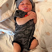 Kyaire is registered to the contest to win money with this photo: newborn, baby, sleeping, onesie, camo_pattern, headband, nike, blanket, animal_print, infant, cozy, peaceful, swaddled, human, skin, foot, hand, indoors, lying_down, cute