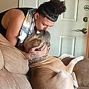 Phoenix is registered to the contest to win money with this photo: person, dog, couch, indoor, love, affection, pet, relaxing, brown_dog, human_dog_interaction, casual_clothing, tattoo, curly_hair, door, home_interior, furniture, comfort, companionship, bond, kiss