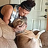 person, dog, couch, indoor, love, affection, pet, relaxing, brown_dog, human_dog_interaction, casual_clothing, tattoo, curly_hair, door, home_interior, furniture, comfort, companionship, bond, kiss
