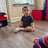 baby, child, toddler, sitting, indoors, portrait, face, wide_eyed, surprised, dark_clothing, socks, wood_floor, window, blinds, toolbox, storage_cube, punching_bag, playroom, home, photography
