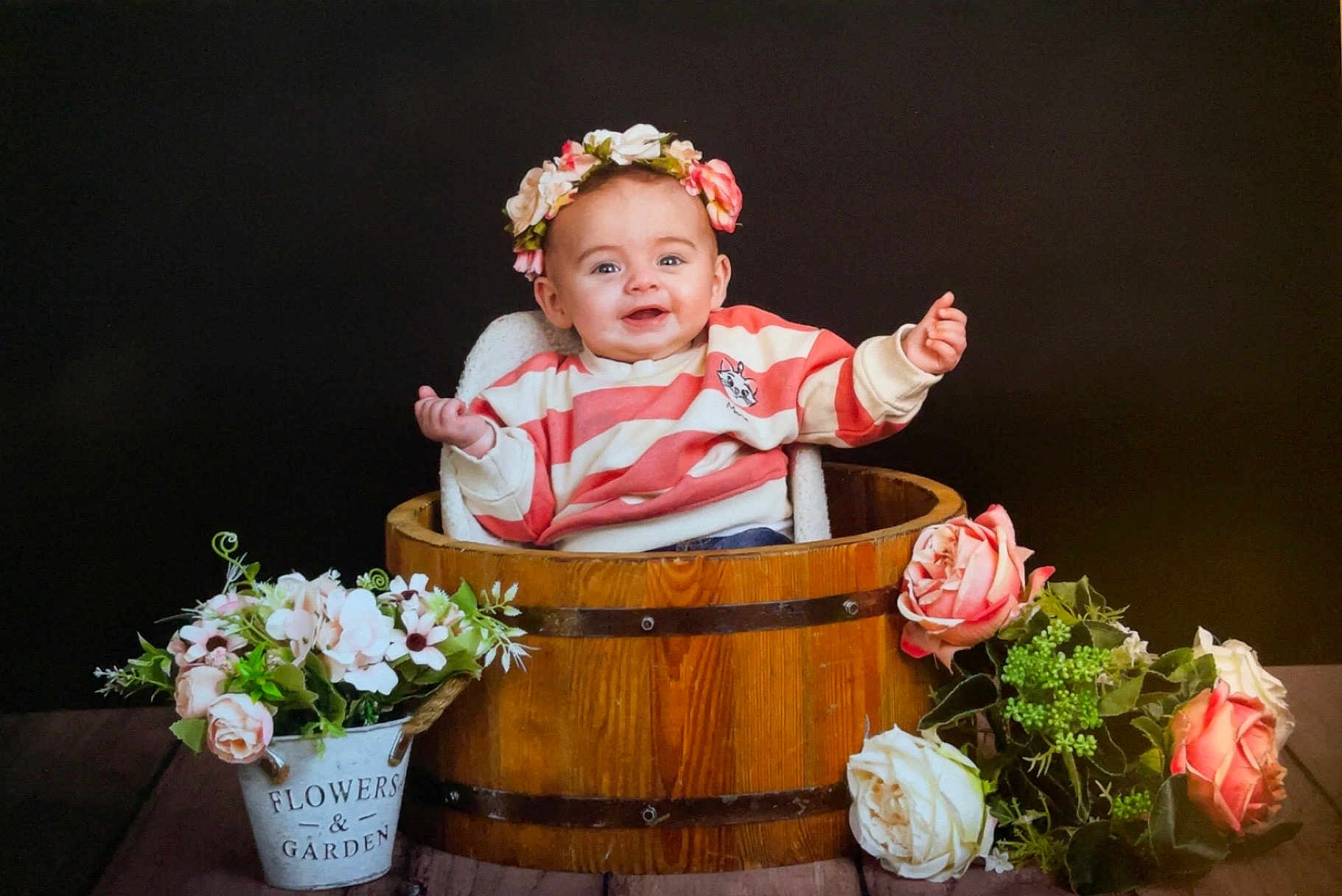Marie participe au concours pour gagner de l'argent avec cette photo : baby, child, cute, decorative, flower_crown, flowers, greenery, happy, indoor, pink_flowers, plant, portrait, pot, sitting, smiling, striped_sweater, white_flowers, wooden_bucket, wooden_surface, young_child
