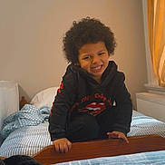 Karter Deqwan Dixon joined the competition — help win amazing prizes! bed, bedding, blanket, child, clothing, cozy, curly_hair, curtain, furniture, happy, hoodie, indoor, person, playful, radiator, room, smile, striped, window, wood