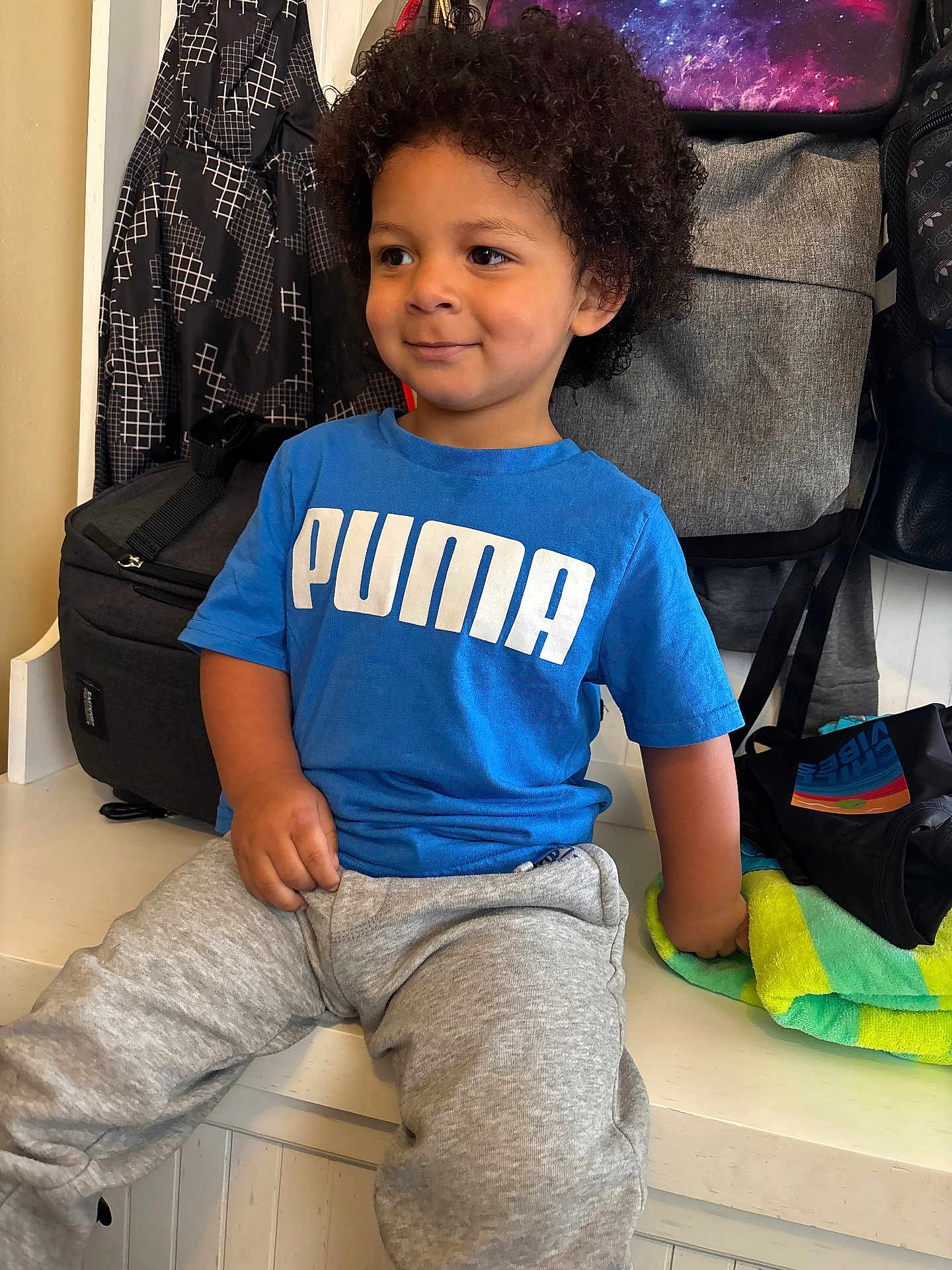 Karter Deqwan Dixon joined the competition — help win amazing prizes! bags, bench, blue_tshirt, casual, child, clothing, curly_hair, daylight, grey_sweatpants, happy, home, indoor, person, portrait, puma_logo, relaxed, seated, smiling, towel, young_child