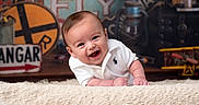 Brayden is registered to the contest to win money with this photo: baby, smiling, white_polo_shirt, blanket, vintage_signs, toy_airplane, lantern, indoor, portrait, child, cute, happy, face, infant, retro, decor, playful, person, closeup, studio